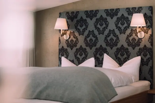 Gemütliches Doppelbett mit elegantem Kopfteil und Nachttischlampen im Naturhotel Chesa Valisa****s.