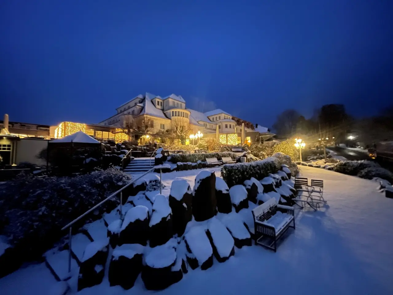 Festlich beleuchtete Aussenansicht des Hotel Heinz im Winter bei Nacht, mit verschneitem Garten und gemütlicher Atmosphäre.