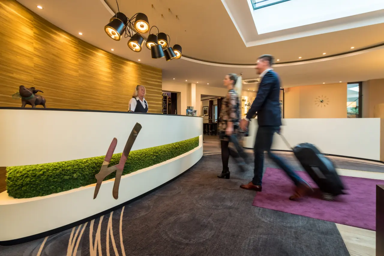 Moderne Rezeption im Hotel Heinz mit freundlicher Mitarbeiterin und ankommenden Gästen.
