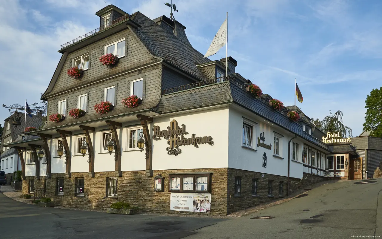 Aussenansicht des Romantik Berghotel Astenkrone mit traditioneller Architektur, Schieferdach und Blumenkästen unter blauem Himmel.