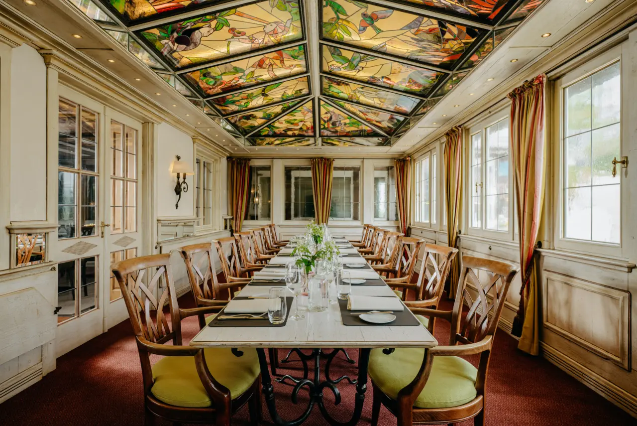 Elegantes Restaurant mit langer Tafel und kunstvoller Buntglasdecke im Romantik Berghotel Astenkrone.