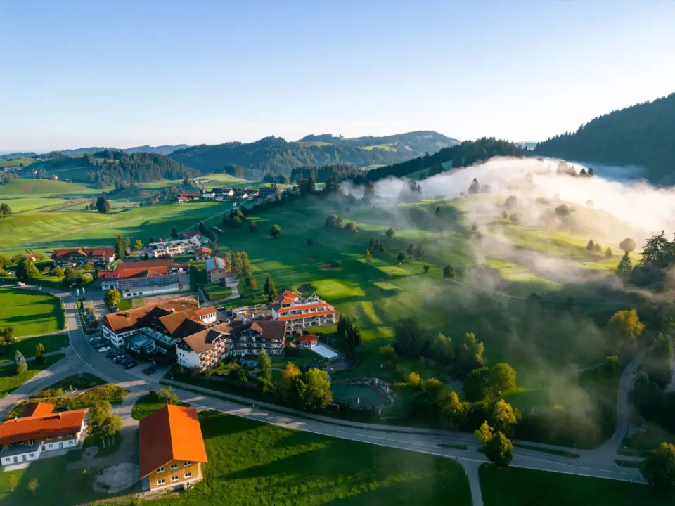 Luftaufnahme des Hotel Dein Engel inmitten einer malerischen Berglandschaft mit Morgennebel und grünen Wiesen.