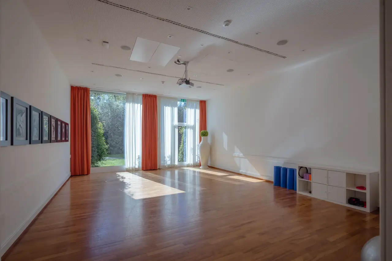 Heller Fitness- und Yogaraum mit Holzboden und großen Fenstern zum Garten im Resort Collina d'Oro.