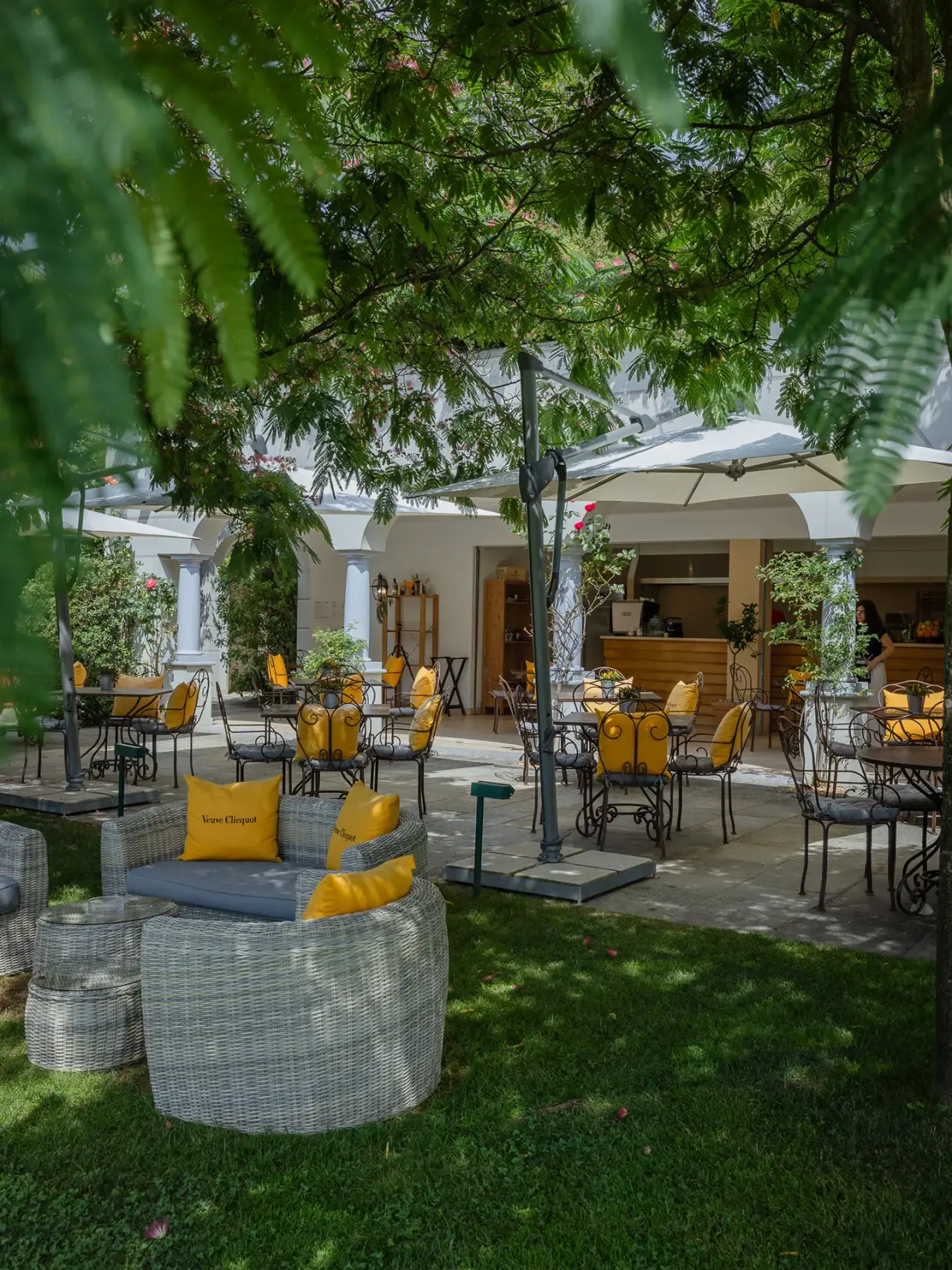 Gemütliche Outdoor-Lounge mit gelben Kissen und Restaurantbereich im grünen Garten des Resort Collina d'Oro.