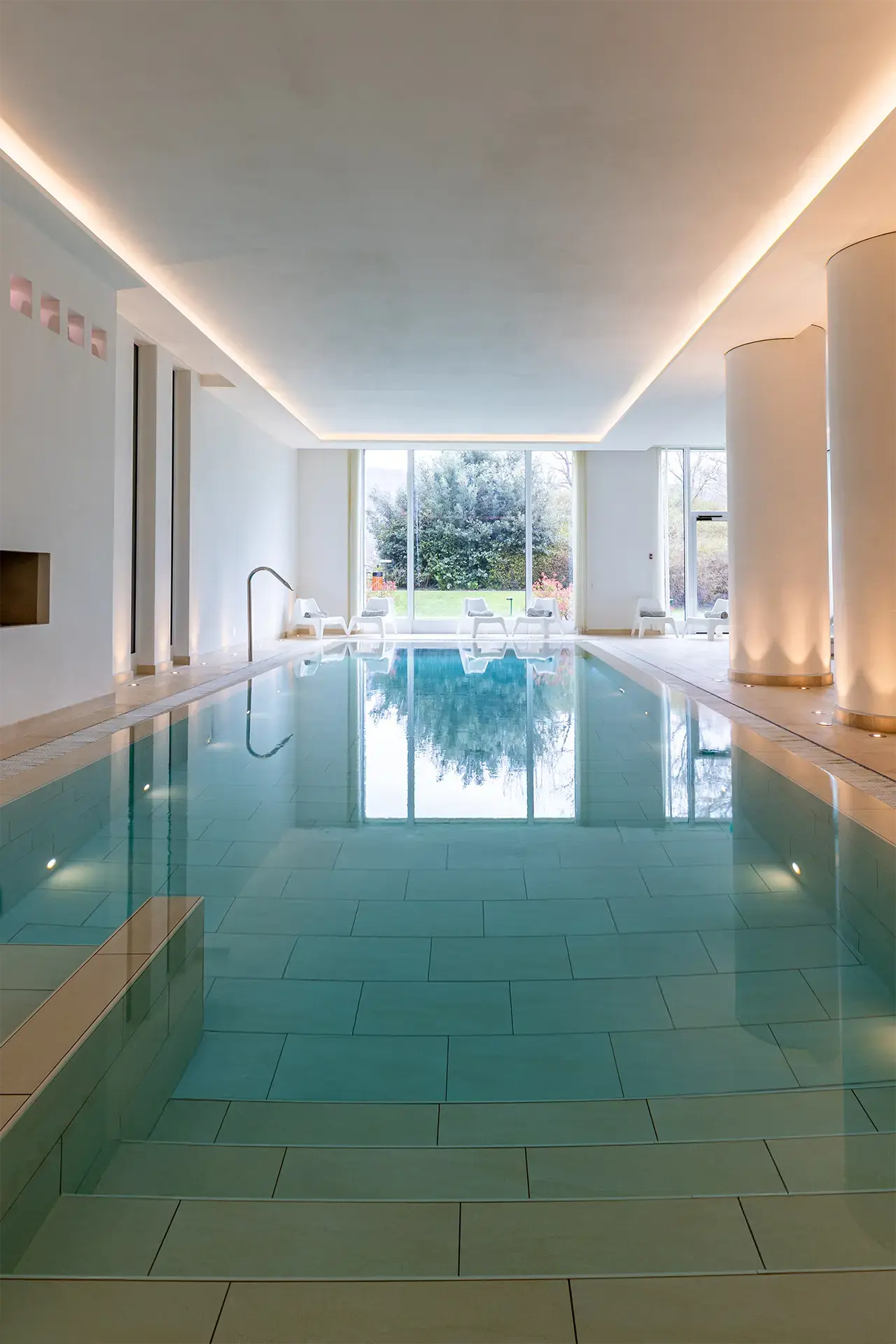 Modernes Hallenbad mit grossen Panoramafenstern und Liegeflächen im Resort Collina d'Oro. Ideal zur Entspannung.