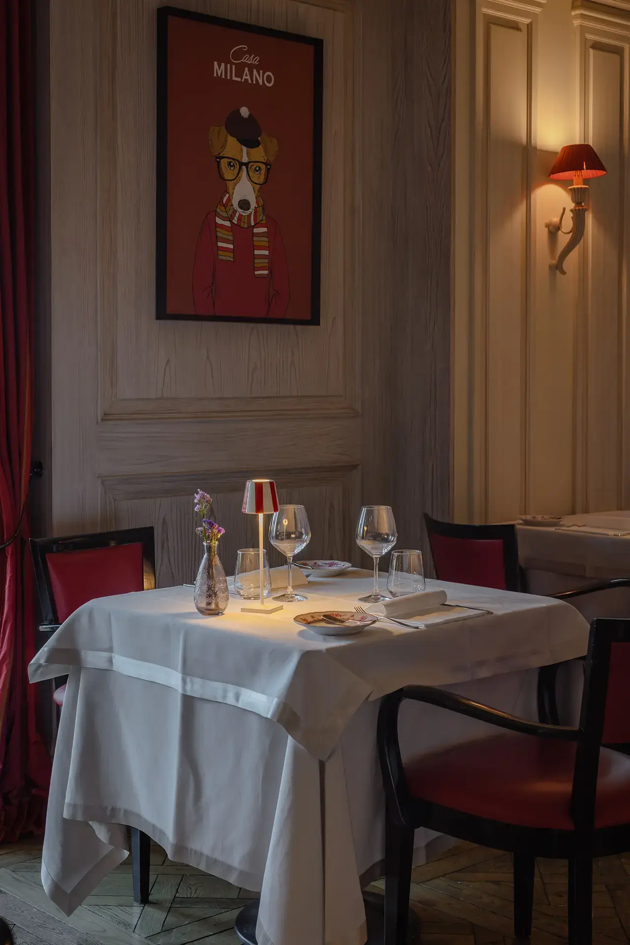 Gemütlich gedeckter Restauranttisch mit rotem Stuhl und Wandbild im Resort Collina d'Oro.