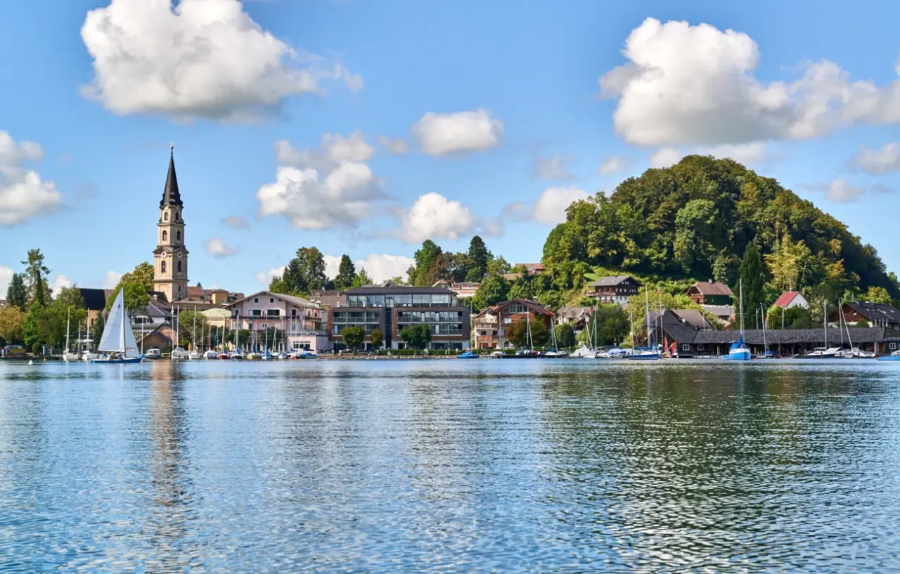 Idyllischer Panoramablick auf Mattsee mit Kirche und Segelboot, die malerische Umgebung des Seewirt Mattsee Kuschelhotel & Spa.