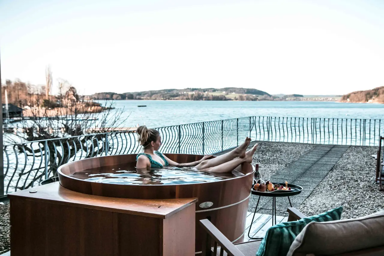 Gast entspannt im Holzbadezuber mit Blick auf den Mattsee im Seewirt Mattsee Kuschelhotel & Spa.