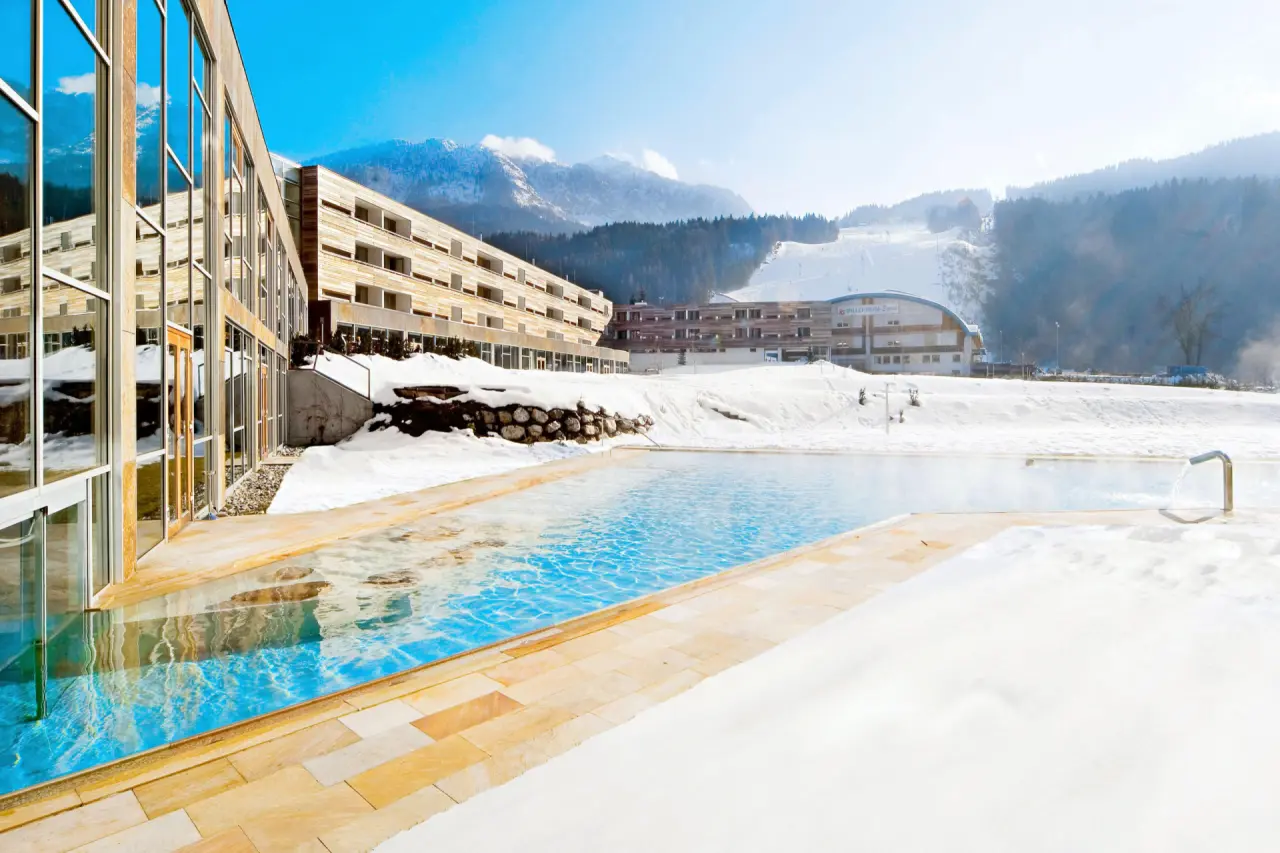 Beheizter Aussenpool im Schnee mit Blick auf die Berge und Skipiste des Falkensteiner Carinzia Hotel.