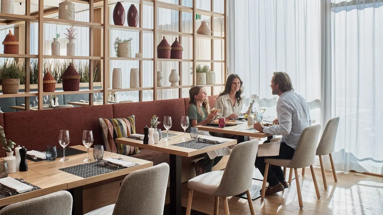 Familie beim Abendessen im modernen Restaurant des Falkensteiner Carinzia Hotels mit stilvoller Einrichtung und Tageslicht.