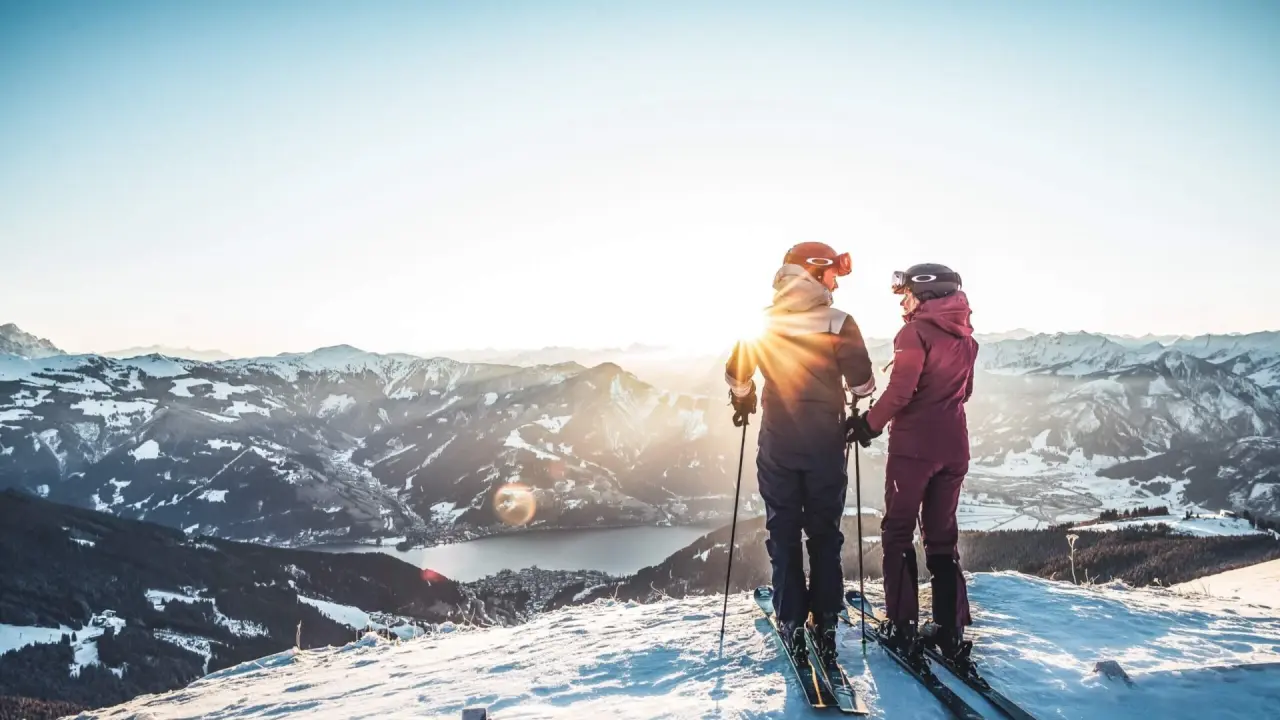 Paar beim Skifahren mit Panoramablick auf verschneite Berge und den Zeller See bei Sonnenuntergang im Hotel Falkenstein Kaprun.