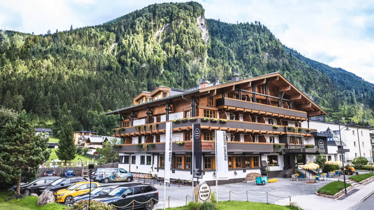 Alpenhotel Das Falkenstein Kaprun mit traditioneller Holzfassade und Balkonen, eingebettet in die grüne Bergwelt.