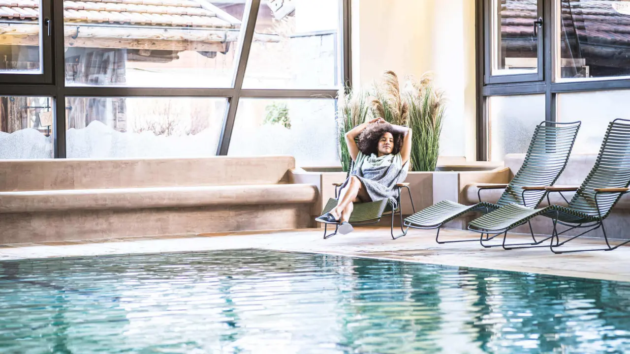 Entspannter Gast am Indoor-Pool mit grossen Fenstern im Wellnessbereich des Hotel Das Falkenstein Kaprun.