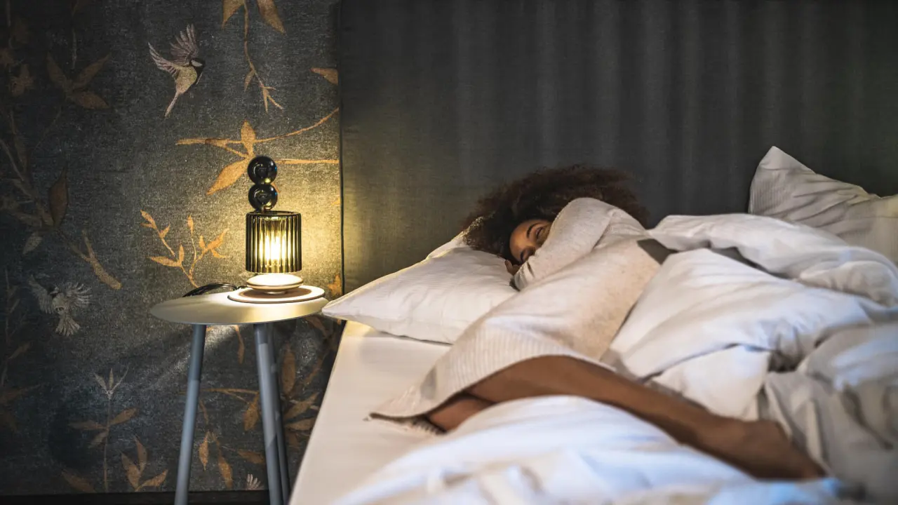 Eine Person schläft entspannt in einem komfortablen Hotelzimmer im Falkenstein Kaprun mit stilvoller Nachttischlampe.