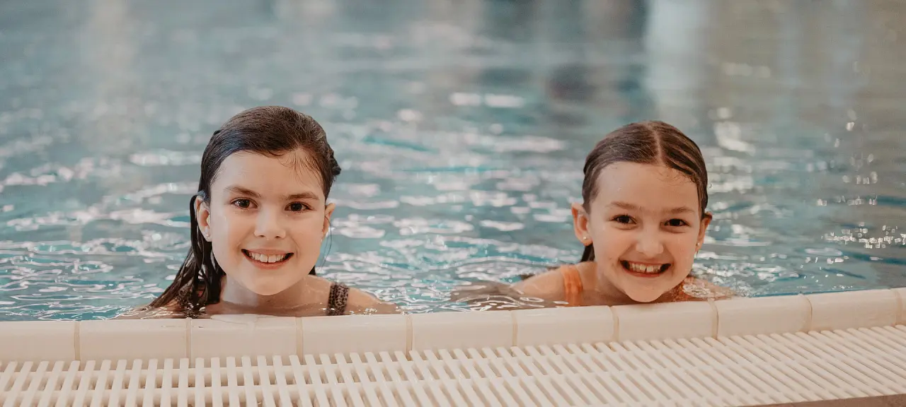 Zwei lachende Kinder im Schwimmbad des Hotel Berghof in St. Johann in Salzburg, die Freude am Familienurlaub zeigen.