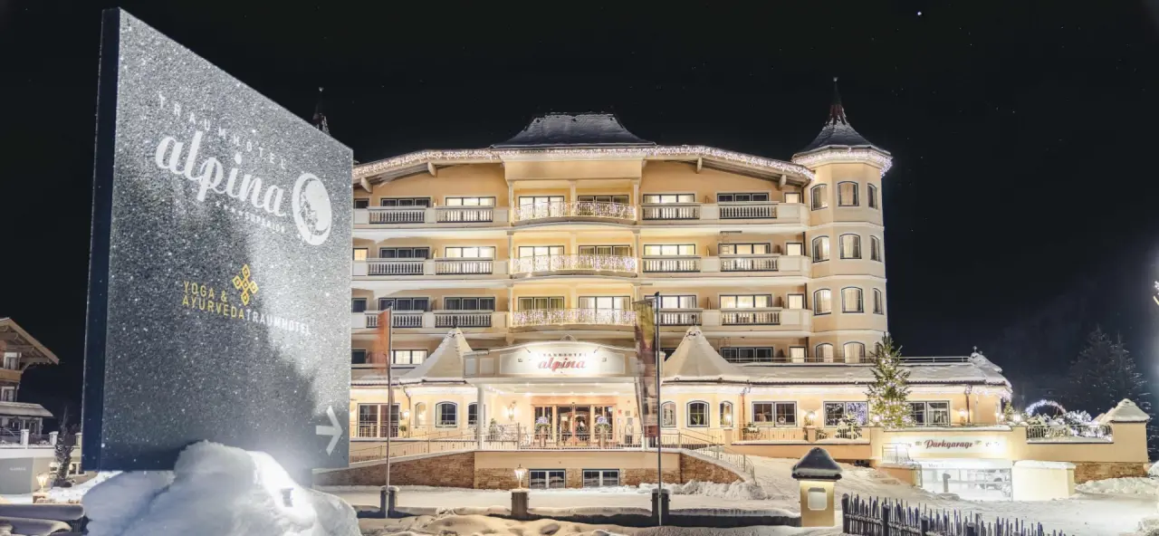 Festlich beleuchtetes Traumhotel Alpina Adults Only im Winter bei Nacht, umgeben von Schnee. Fokus auf Yoga & Ayurveda.