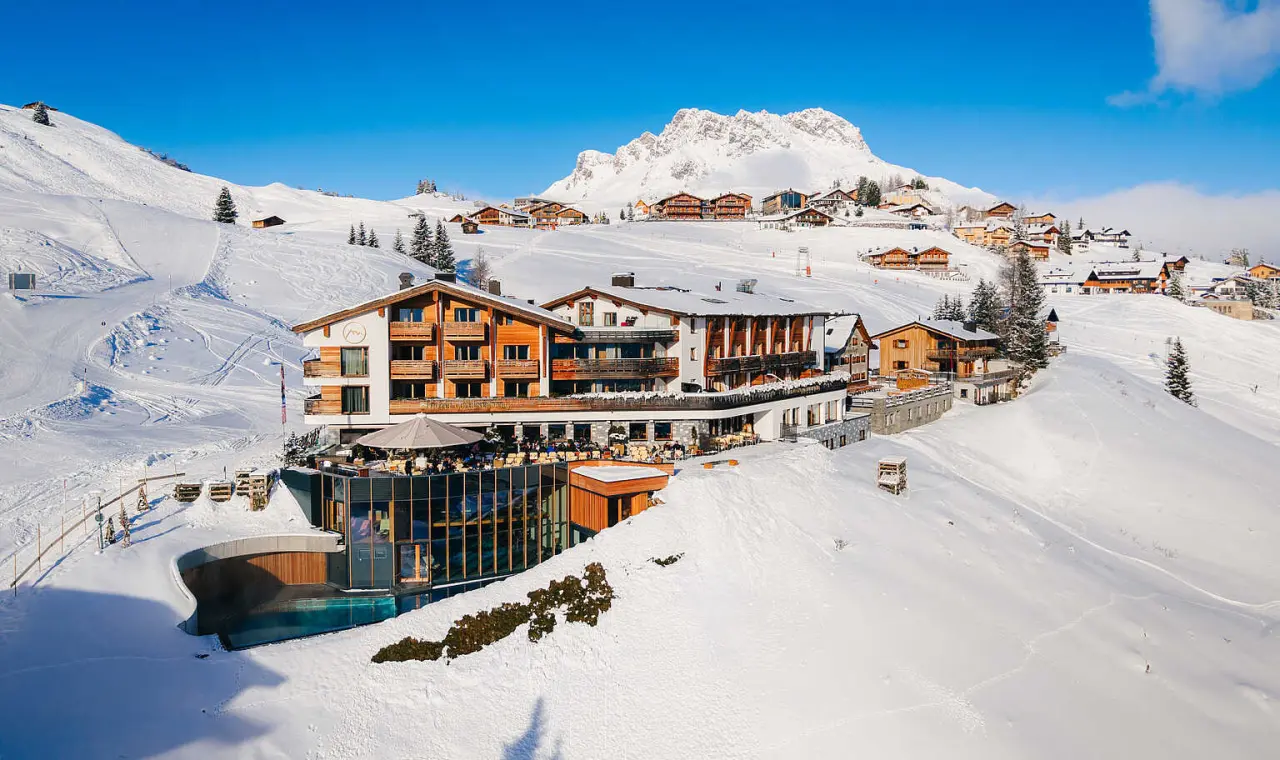 Winteransicht des Hotel Goldener Berg mit verschneiten Bergen, Skipisten und Aussenpool in Oberlech.