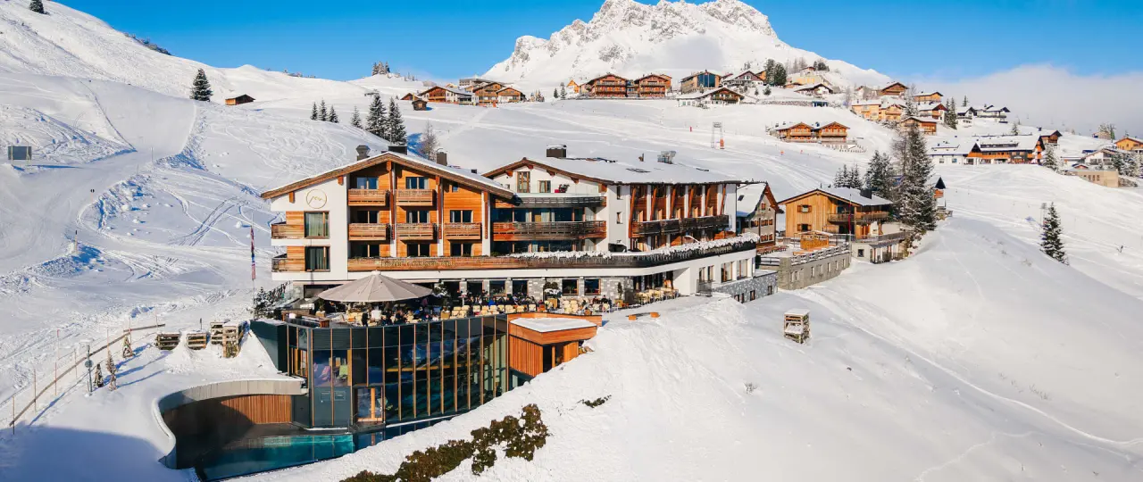 Winterpanorama des Hotel Goldener Berg in Lech am Arlberg, umgeben von verschneiten Bergen und Skipisten, mit Aussenpool.