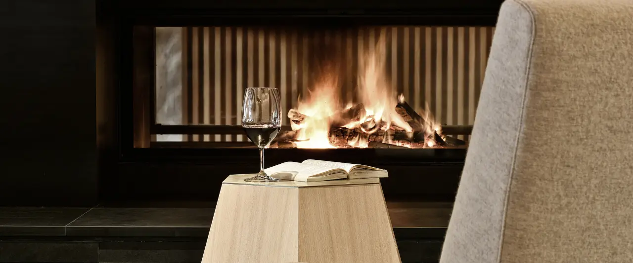Gemütlicher Abend am Kamin mit Rotwein und Buch im Hotel Goldener Berg. Perfekt für Selfcare und Entspannung.