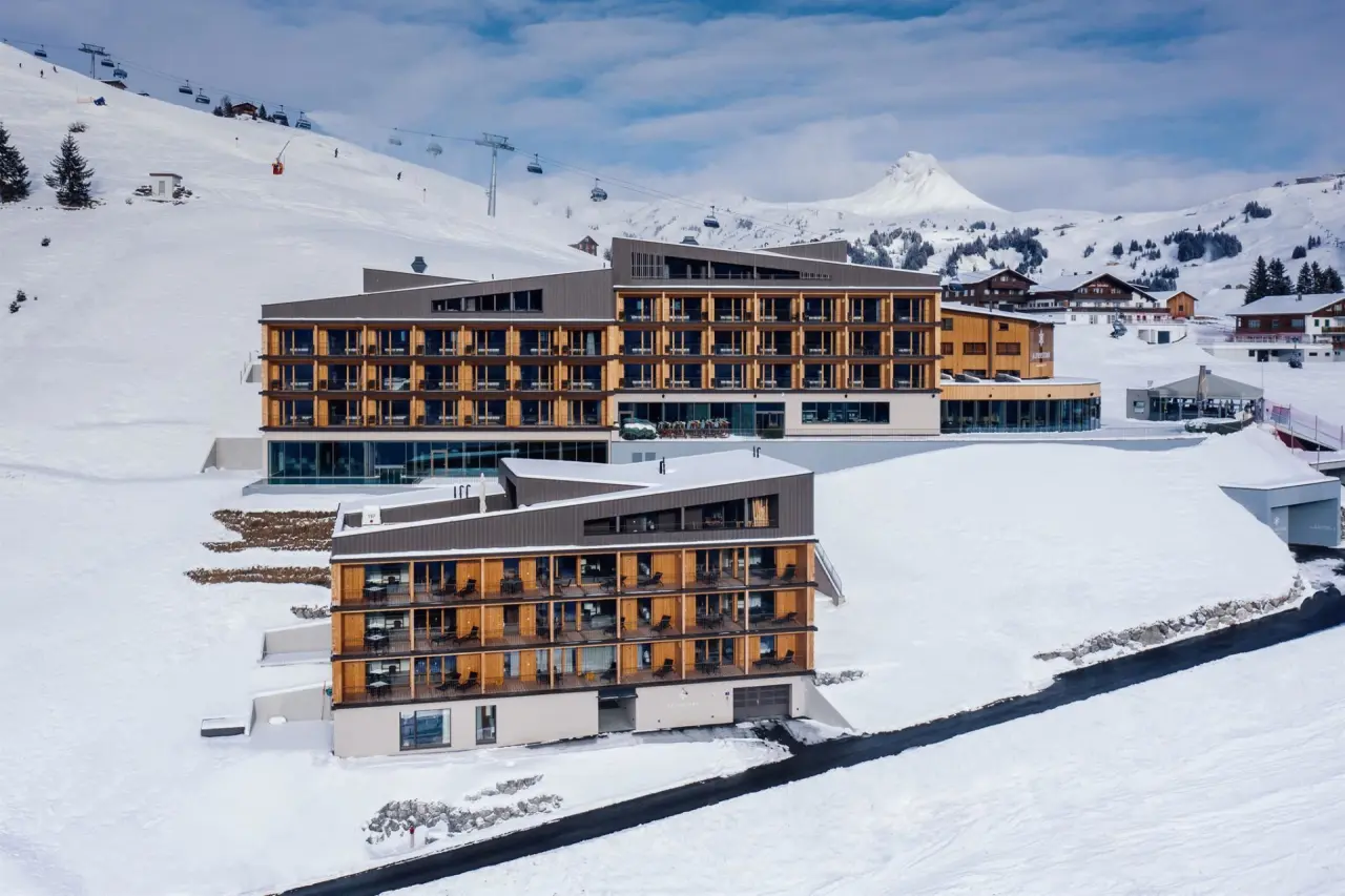 Modernes Alpenstern Panoramahotel im Winter, eingebettet in verschneite Berglandschaft mit Skipisten und Liften.