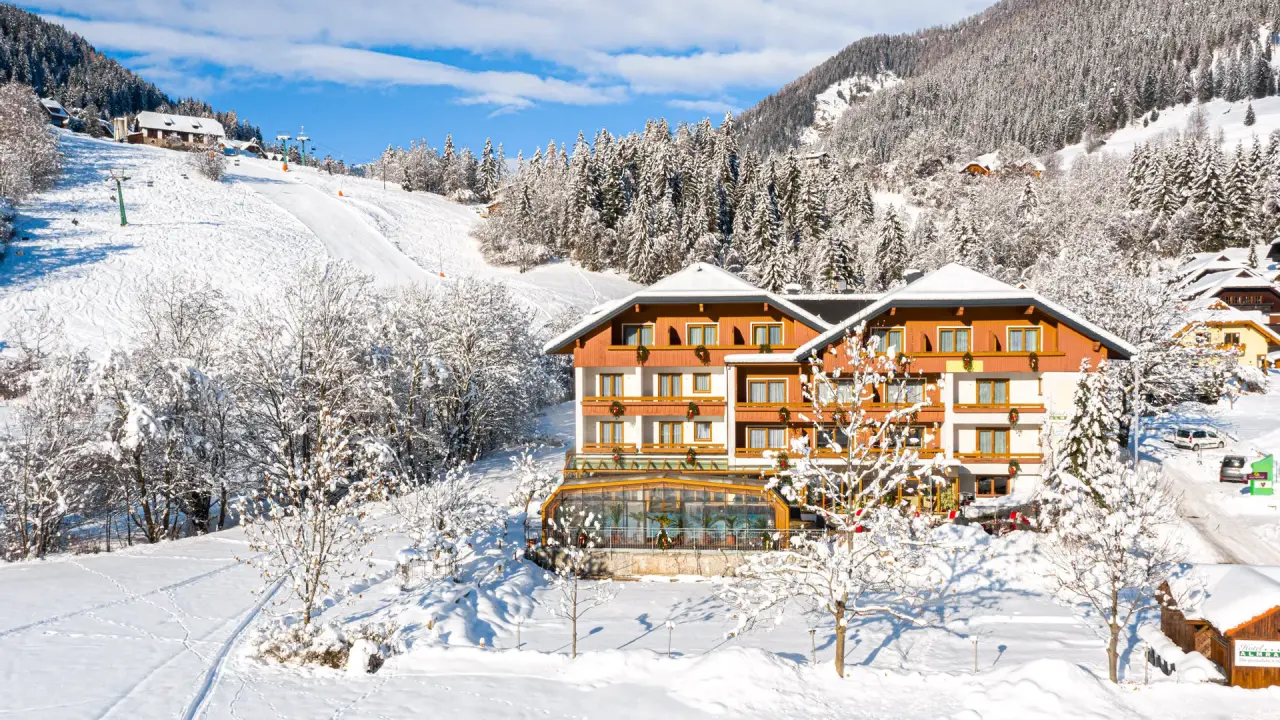 Genusshotel Almrausch im Winter: Hotel direkt an der Skipiste mit verschneiter Berglandschaft und blauem Himmel.
