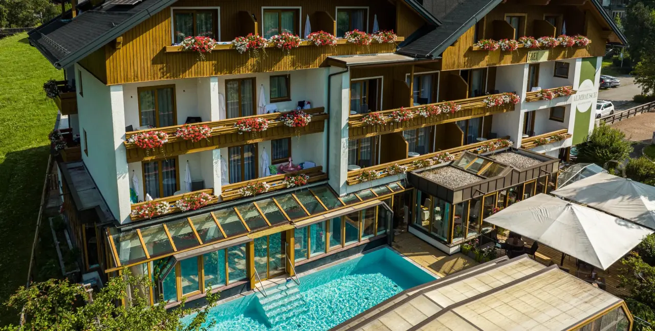 Genusshotel Almrausch: Aussenansicht mit Balkonen voller Blumen und einladendem Aussenpool unter Glasdach.