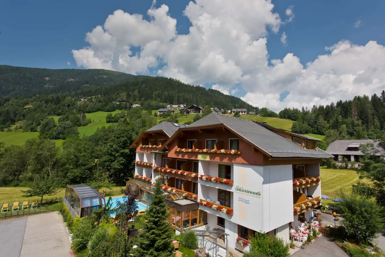 Aussenansicht des Genusshotel Almrausch mit Poolbereich und Alpenpanorama an einem sonnigen Tag.
