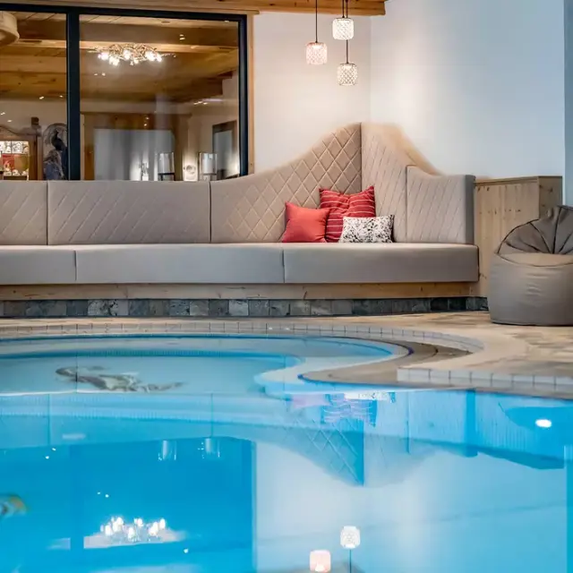 Gemütlicher Innenpool mit bequemer Lounge-Sitzbank und Holzelementen im Alpenromantik Hotel Wirlerhof.