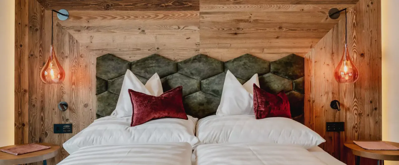 Gemütliches Doppelzimmer mit Holzwand, gepolstertem Kopfteil und warmen Leuchten im Alpenromantik Hotel Wirlerhof.