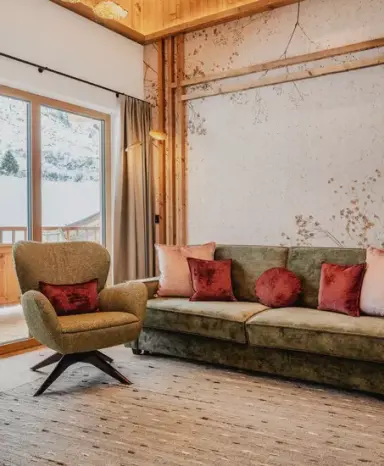 Gemütlicher Wohnbereich im Alpenromantik Hotel Wirlerhof mit Sofa, Sessel und Blick auf die Winterlandschaft.