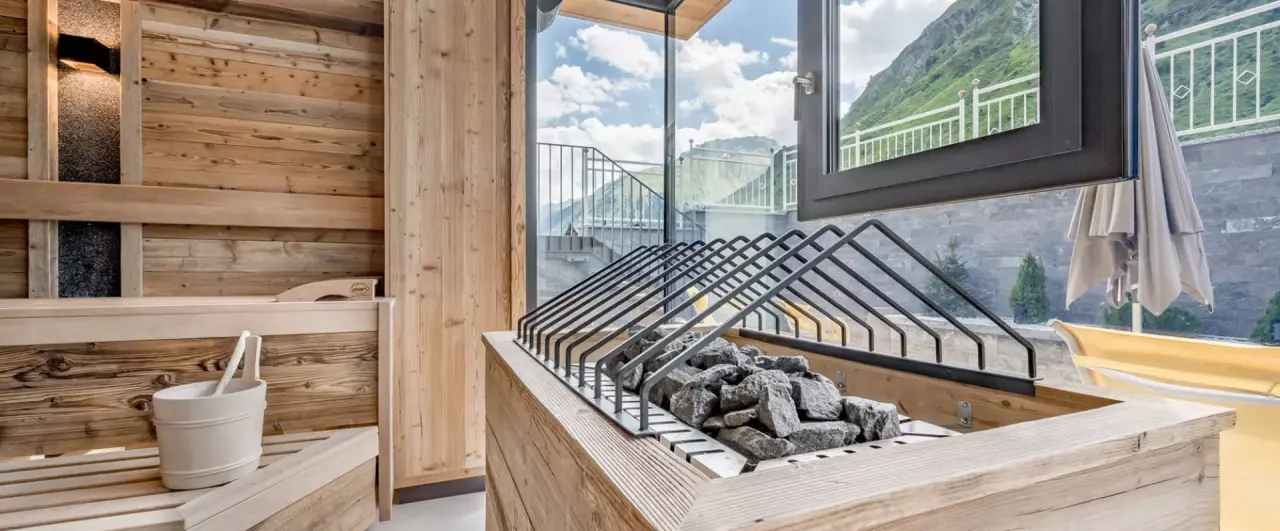 Moderne Panoramasauna mit Bergblick im Alpenromantik Hotel Wirlerhof. Holzsauna mit grossen Fenstern und Natursteinen.