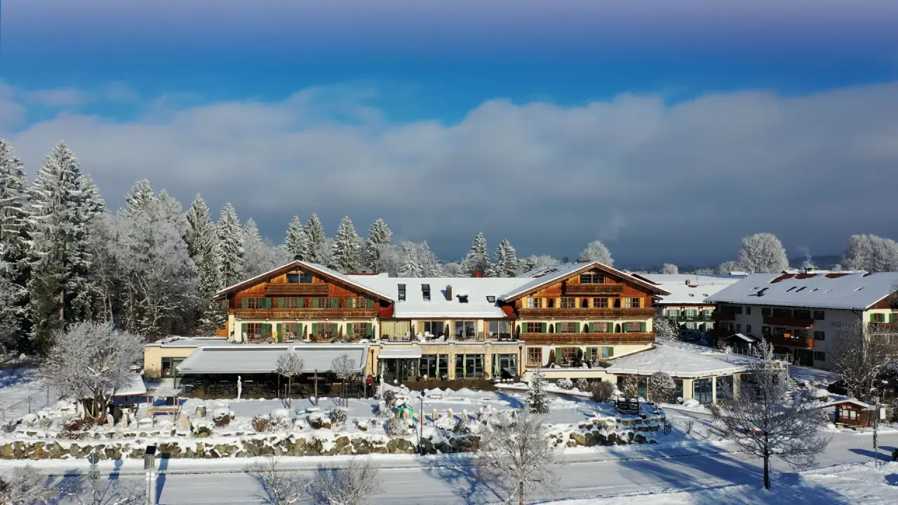 Winterliche Aussenansicht des Parkhotel am Soier See, umgeben von verschneiten Bäumen unter strahlend blauem Himmel.