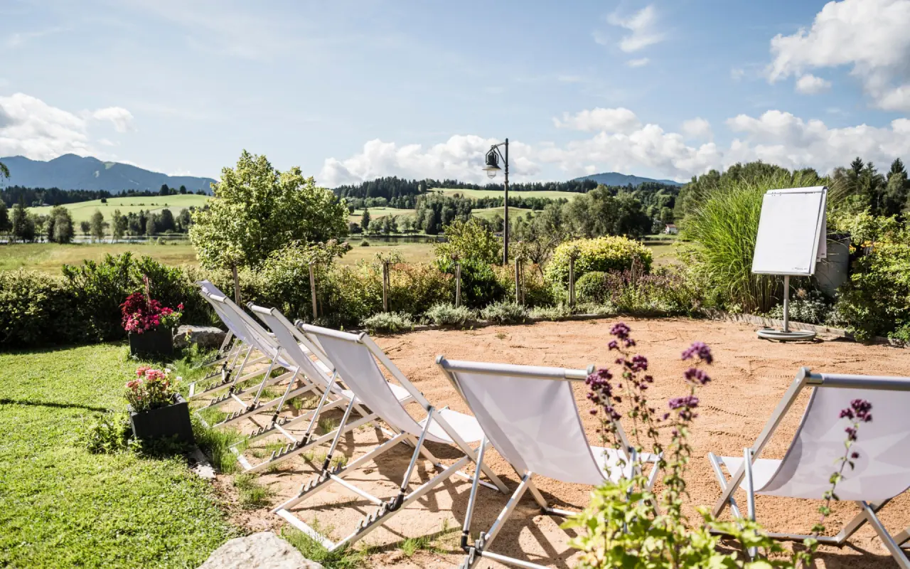 Entspannungsbereich im Garten des Parkhotel am Soier See mit Liegestühlen, Blick auf den See und die bayerischen Berge.