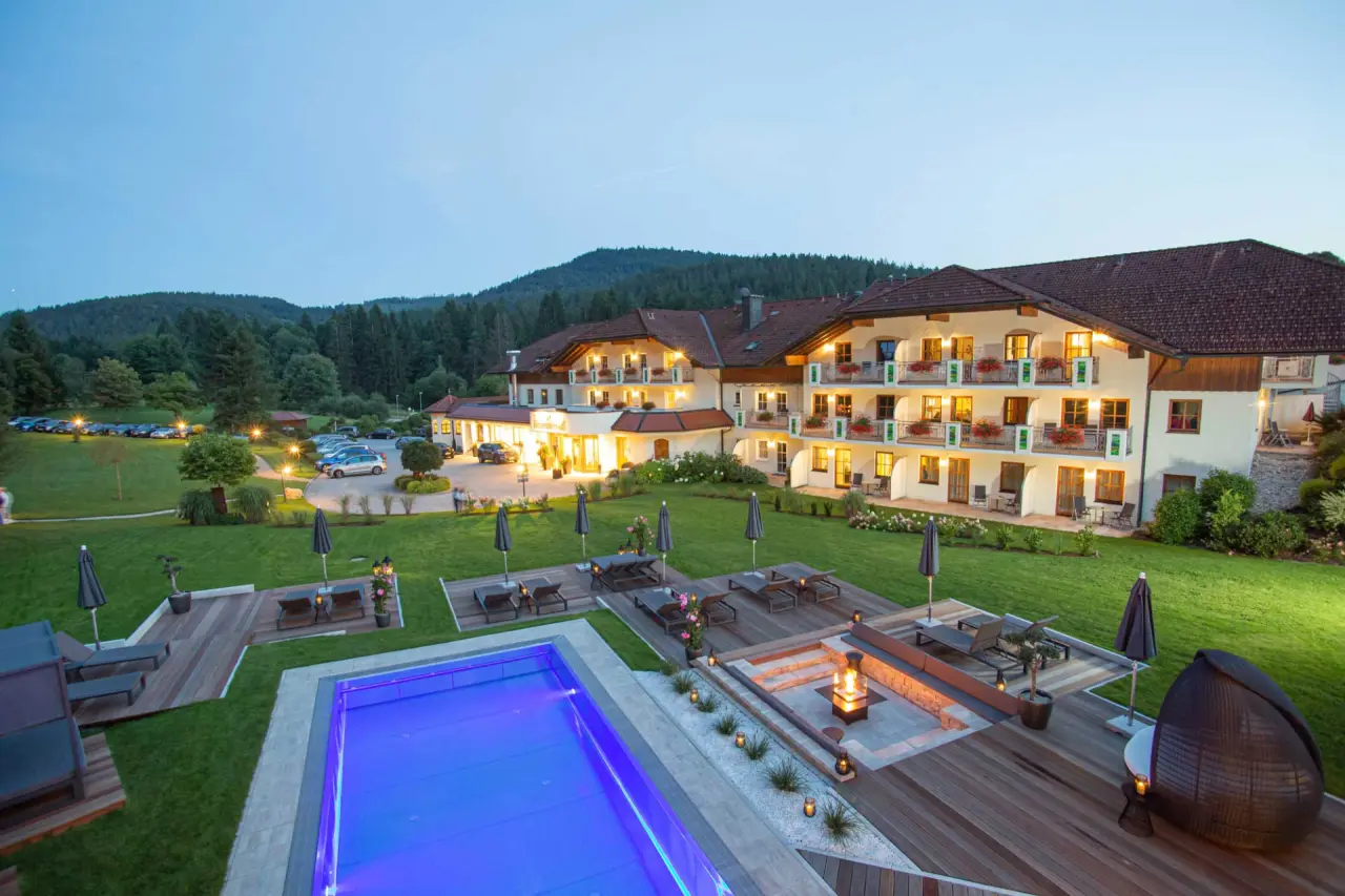Abendliche Aussenansicht des Hotel Hammerhof mit beleuchtetem Pool, Sonnenterrasse und malerischer Berglandschaft.