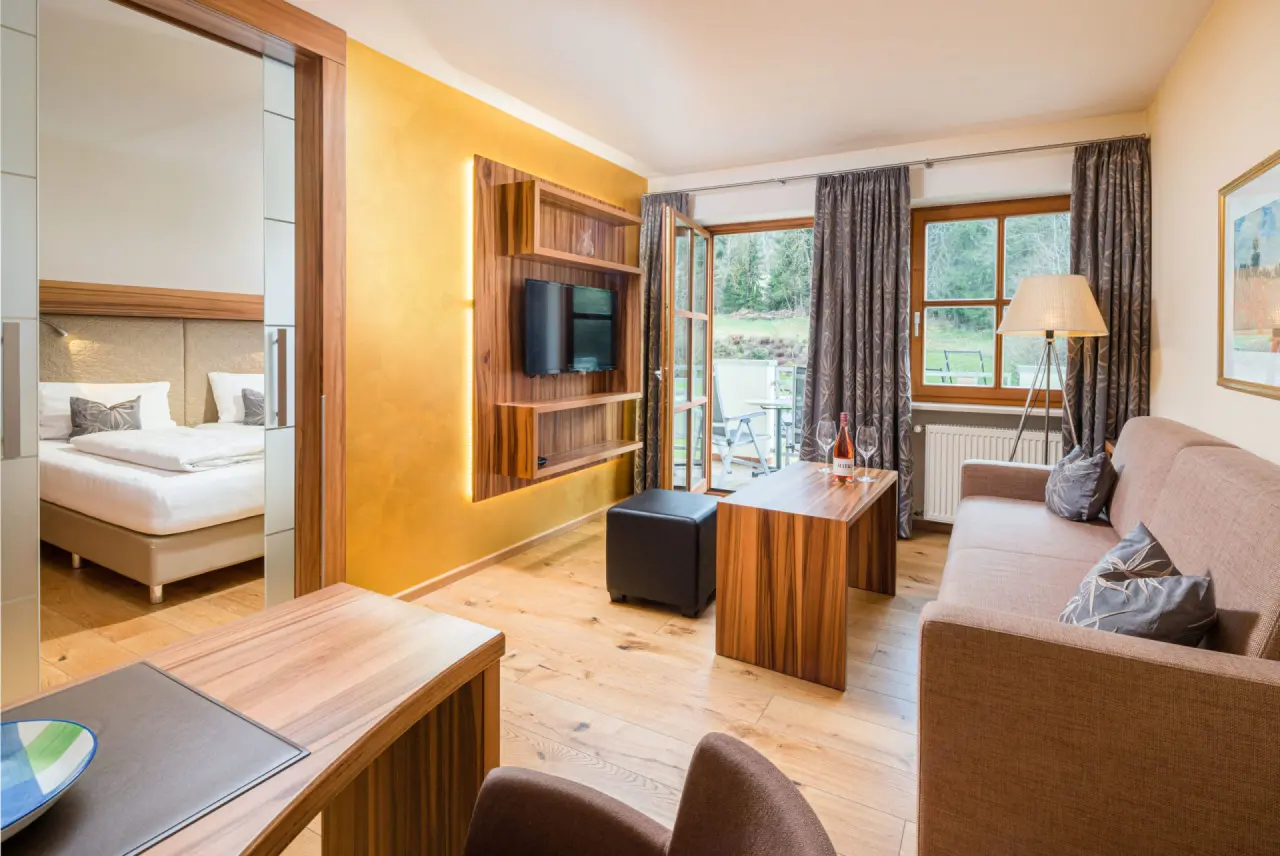 Geräumige Suite im Hotel Hammerhof mit gemütlichem Wohnbereich, Schlafzimmer und Balkon mit Waldblick.