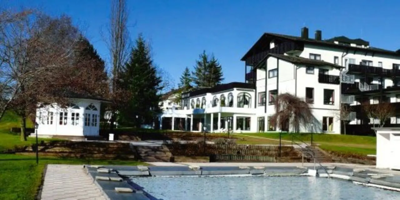 Aussenansicht des Hotel Tanneck Golf & Spa mit Hotelgebäude, Garten und bedecktem Aussenpool bei blauem Himmel.