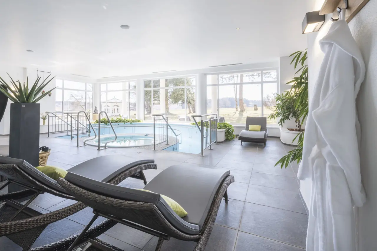 Heller Innenpool mit Whirlpool und Liegebereich im Wellnessbereich des Tanneck Golf & Spa Hotels mit Blick ins Grüne.