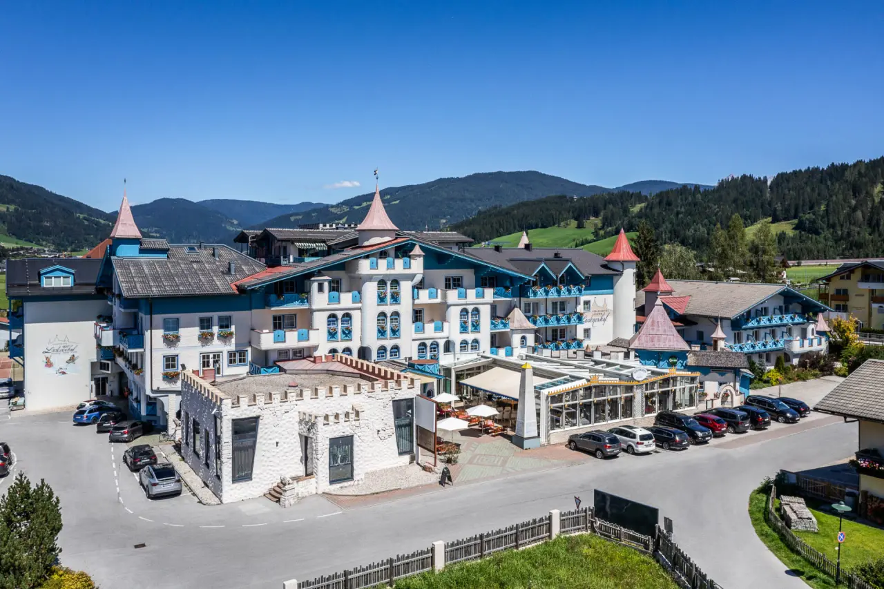 Luftaufnahme des Schlosshotel Lacknerhof****S in den Bergen, umgeben von grünen Wiesen und Wäldern unter blauem Himmel.