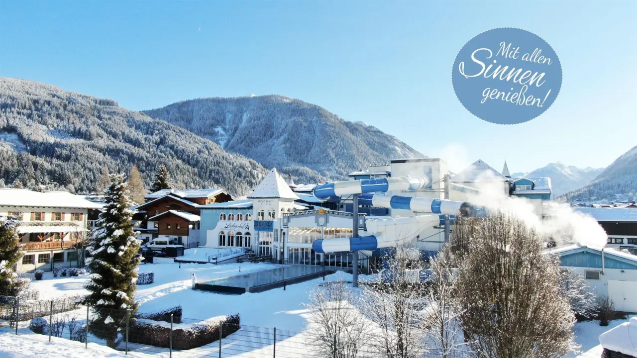 Winteransicht Schlosshotel Lacknerhof****S mit verschneiten Bergen, Aussenpool und Wasserrutschen in Flachau.