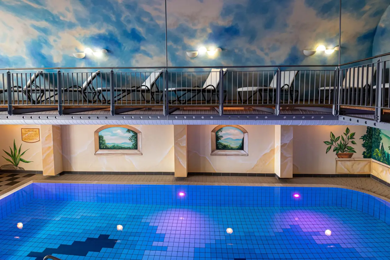 Innenpool mit blauer Beleuchtung und Entspannungsliegen auf der Galerie im Wellnesshotel Randsbergerhof.