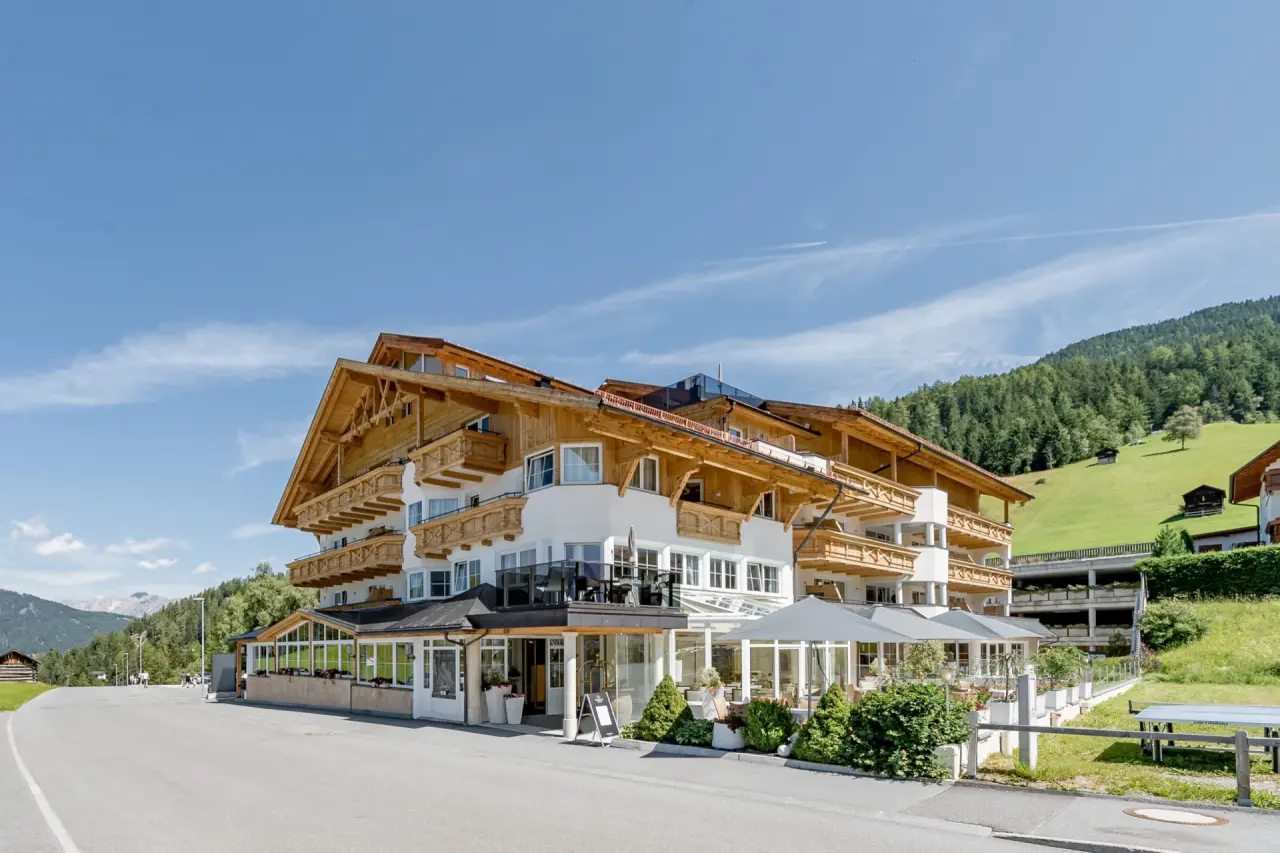 Aussenansicht des Hotel Andy mit traditioneller Holzarchitektur und Balkonen, umgeben von grünen Bergen unter blauem Himmel.