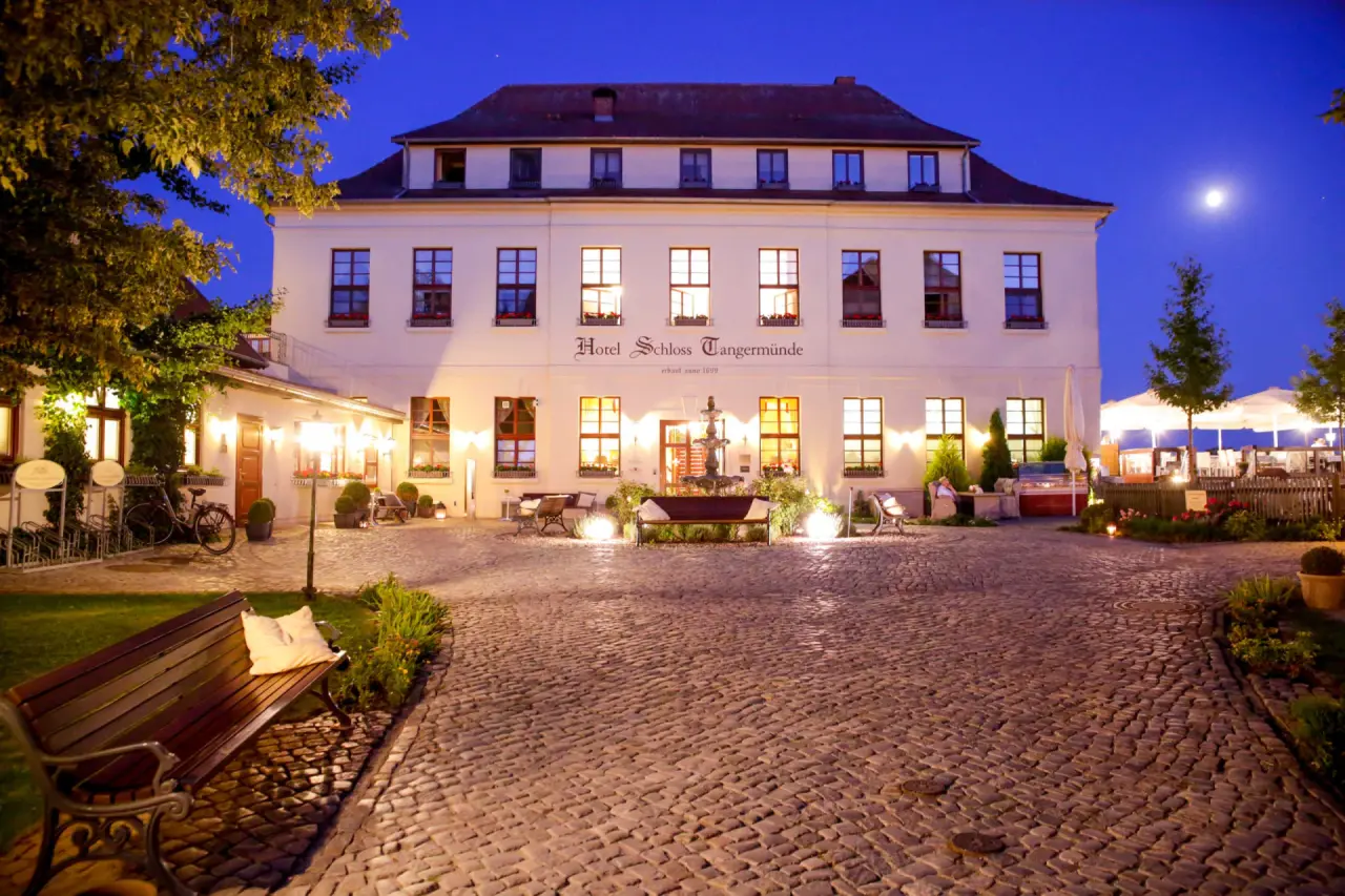 Beleuchtete Fassade des Hotel Schloss Tangermünde bei Nacht, mit charmantem Innenhof, Aussenbestuhlung und Mond am Himmel.