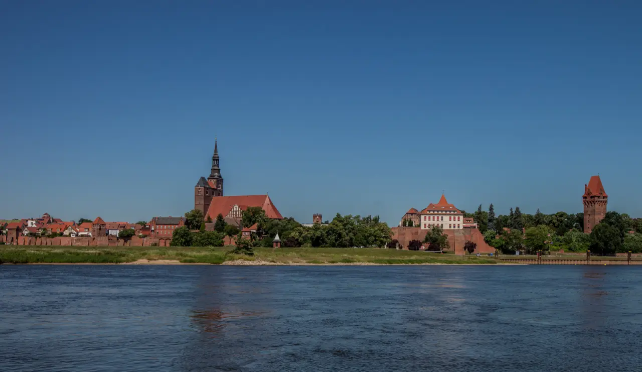 Panoramablick auf das historische Hotel Schloss Tangermünde und die Stadt an der Elbe unter blauem Himmel.