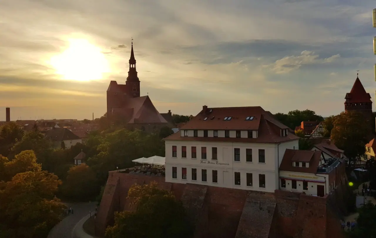 Historisches Hotel Schloss Tangermünde mit Kirchturm und Stadtansicht im warmen Abendlicht bei Sonnenuntergang.