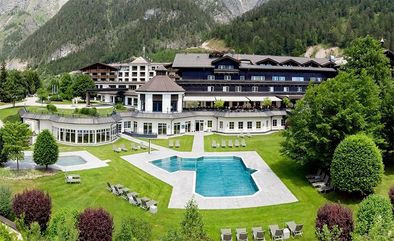 Luftaufnahme des Hotel Gut Brandlhof mit weitläufiger Gartenanlage, Außenpools und majestätischer Bergkulisse.