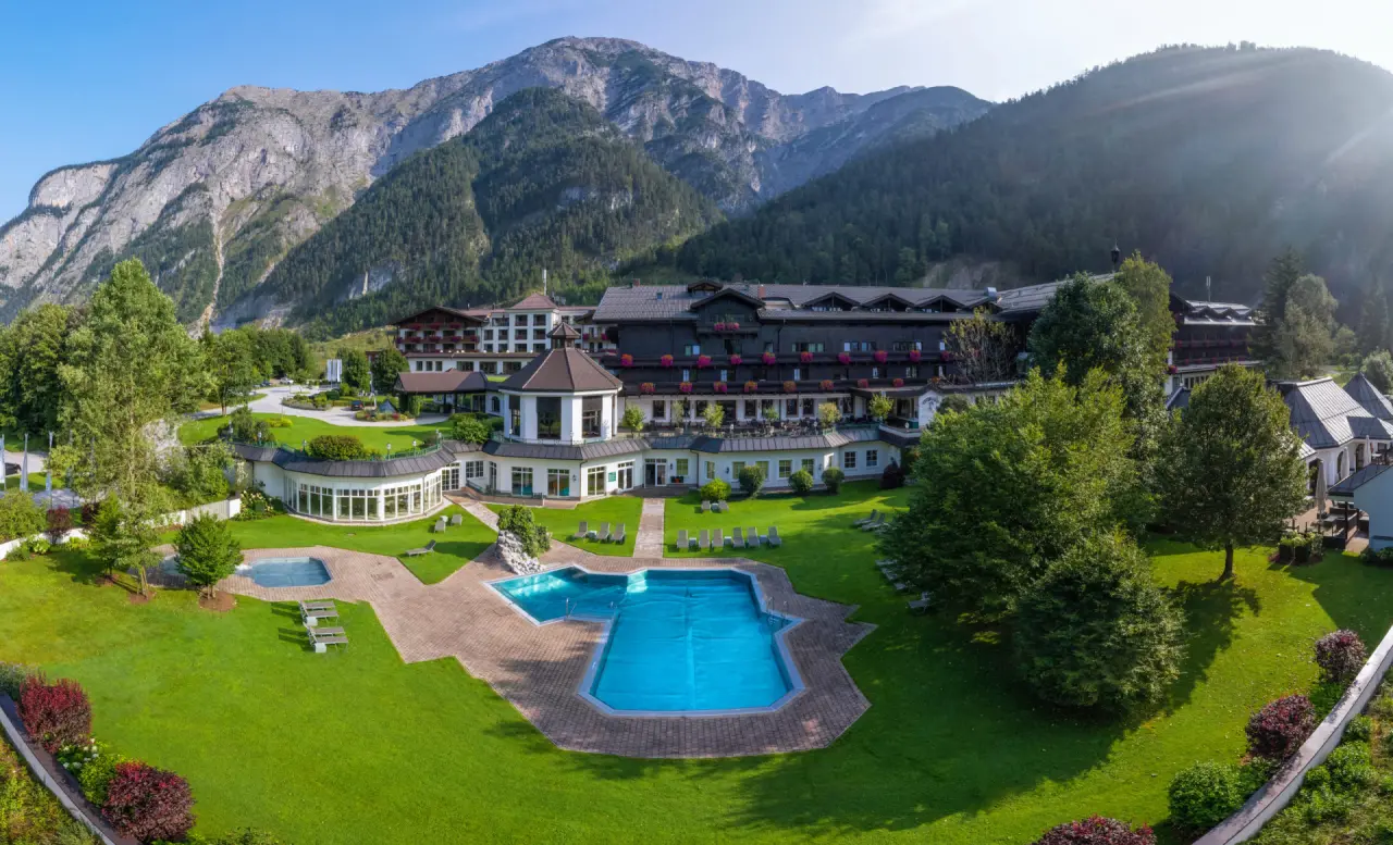 Panoramablick auf das Hotel Gut Brandlhof mit Aussenpools, weitläufigem Garten und majestätischer Bergkulisse.