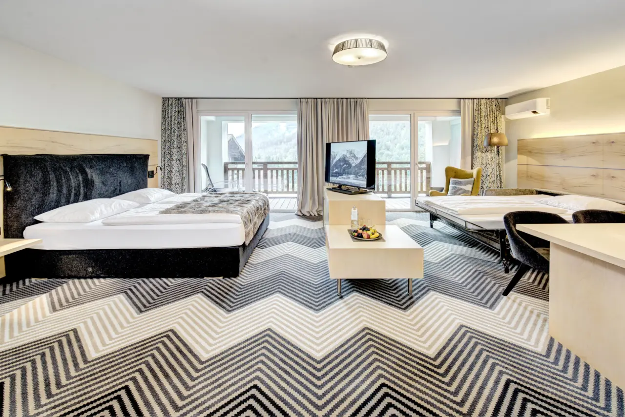 Geräumiges Hotelzimmer im Hotel Gut Brandlhof mit Doppelbett, Schlafsofa, Balkon und Bergblick auf die Alpen.