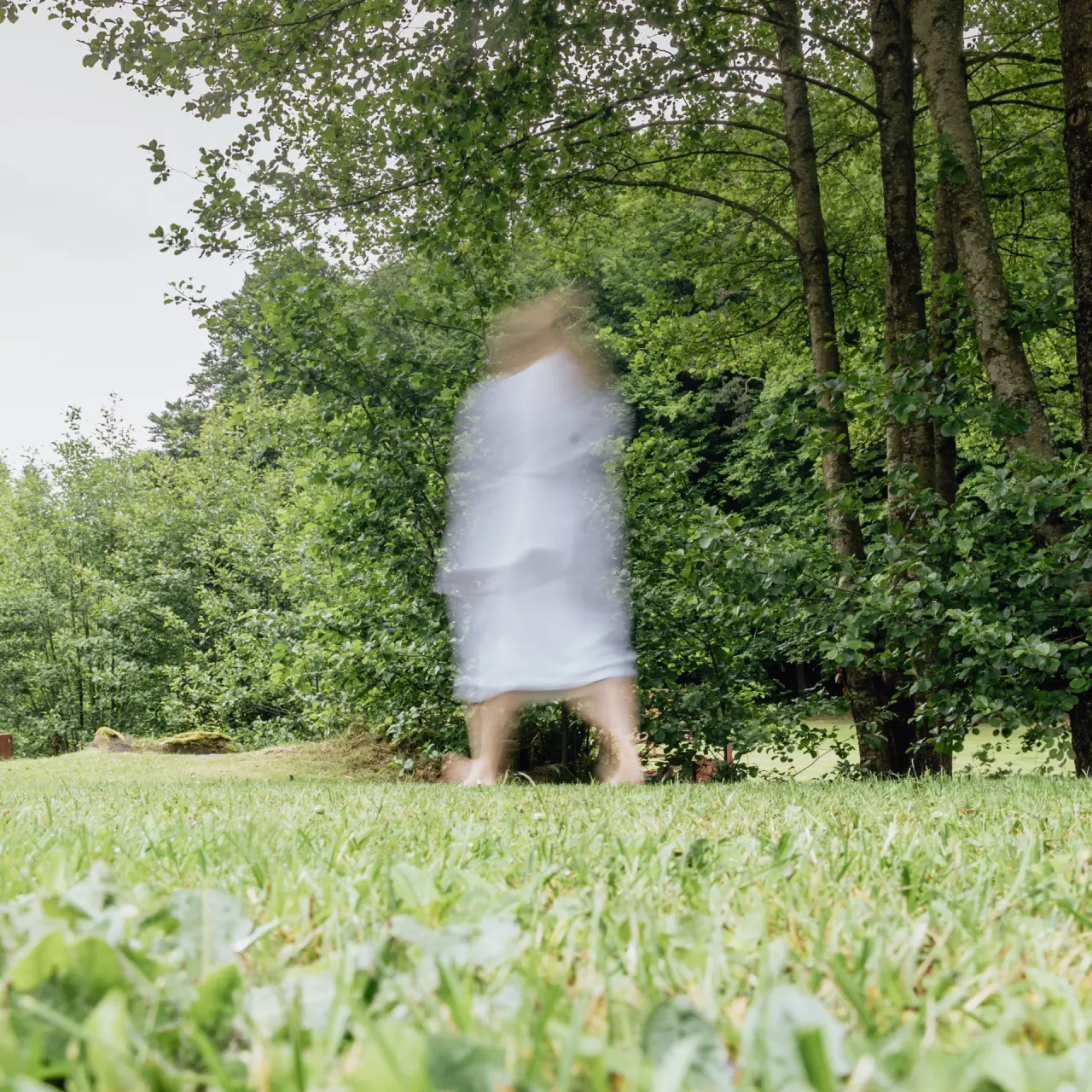 Verschwommene Person im Bademantel barfuss im grünen Garten des Hotel Im Krummbachtal.