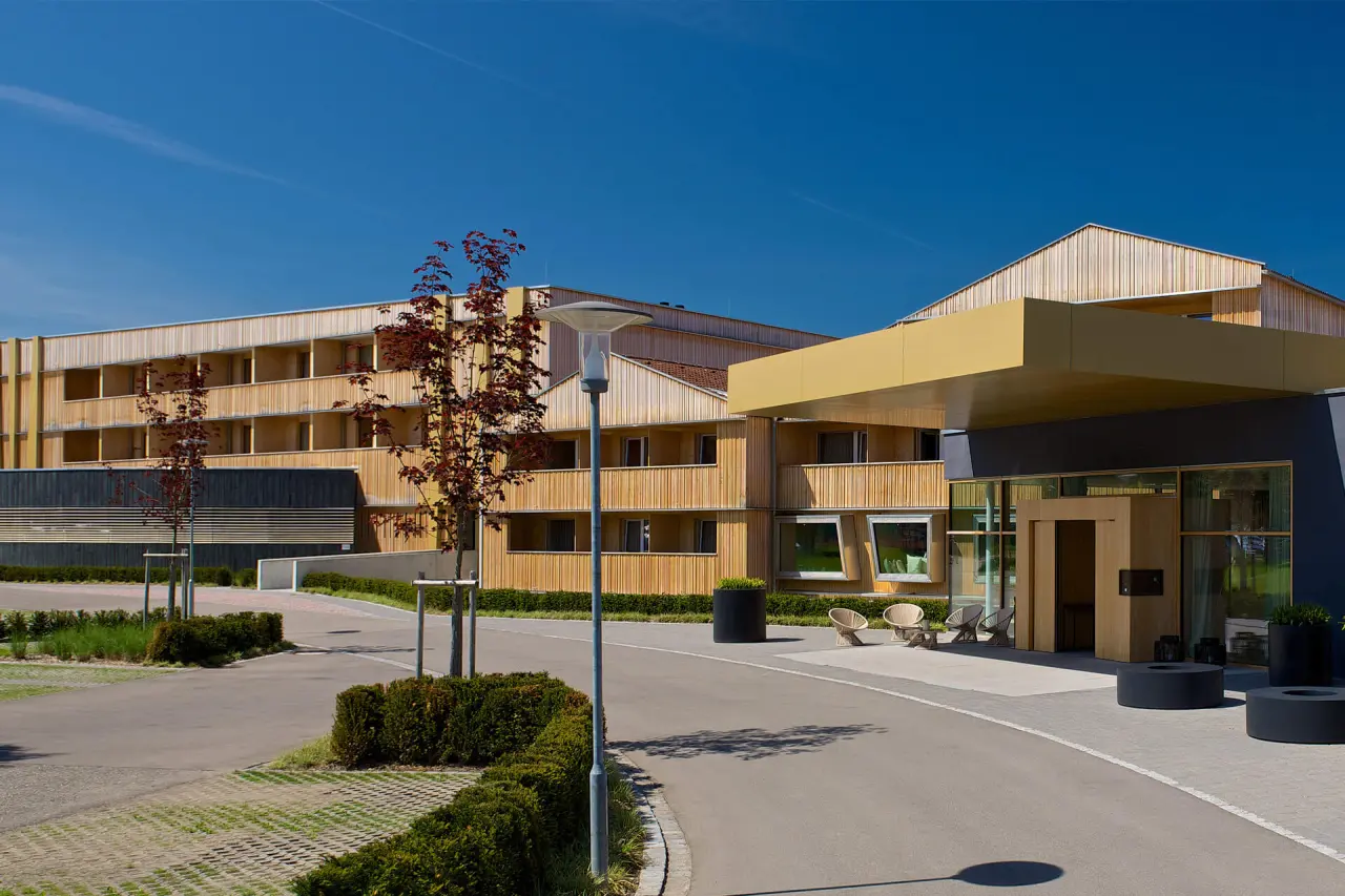 Moderne Holzfassade des Hotels Tannenhof Sport & SPA mit Eingangsbereich und Zufahrt unter blauem Himmel.