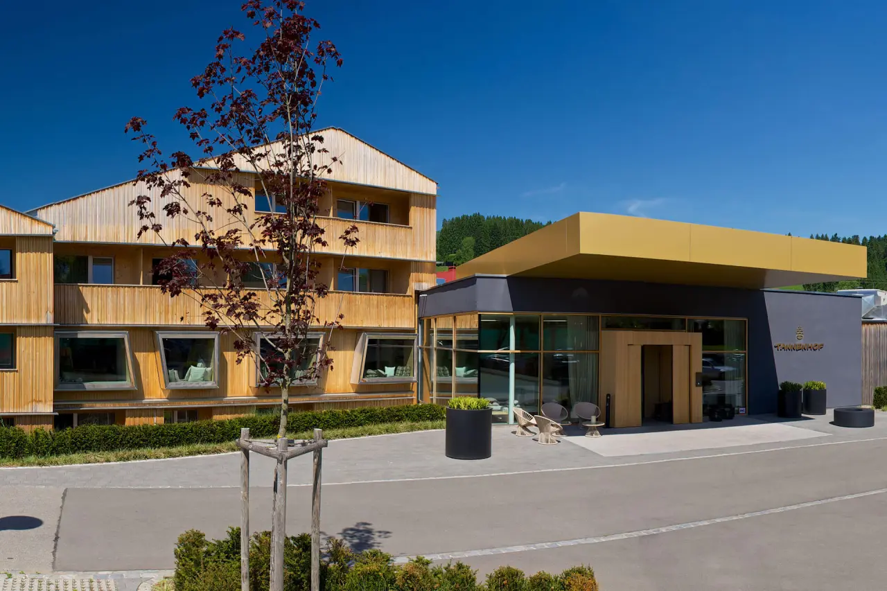 Moderne Aussenansicht des Tannenhof Sport & SPA Hotels mit Holzfassade und Eingangsbereich unter blauem Himmel.